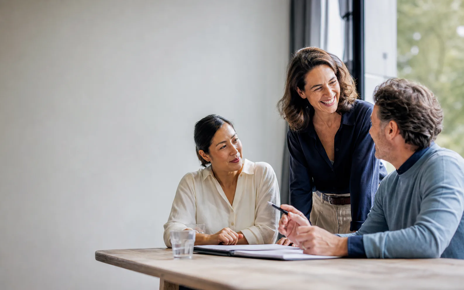 Drie professionals werken met zichtbaar plezier samen aan een tafel bij het raam